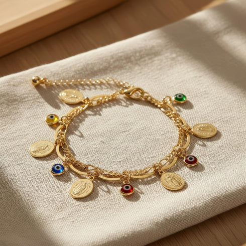 A 14k gold-filled bracelet with colored enamel evil eye beads and Mary Virgin charm, displayed on a beige textured cloth.