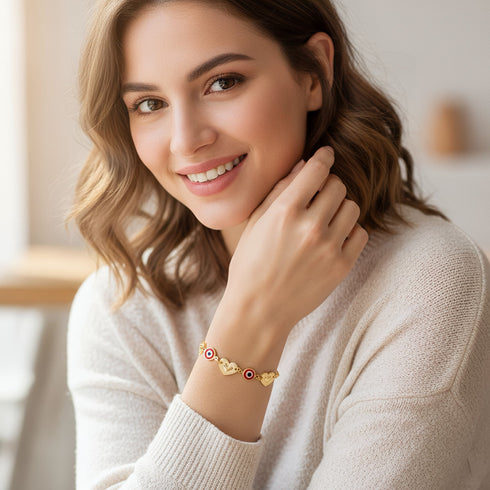 Smiling woman in a cream sweater shows off a Red Evil Eye Charm Bracelet with red accents, worn as a stylish protective talisman.