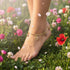 A foot with a 14k Gold-filled Anklet stands on grass among colorful flowers and falling petals in bright sunlight.