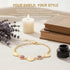 A gold Heart Rolo Link bracelet with heart and circular charms rests among books, lavender, a candle, and an ink bottle.