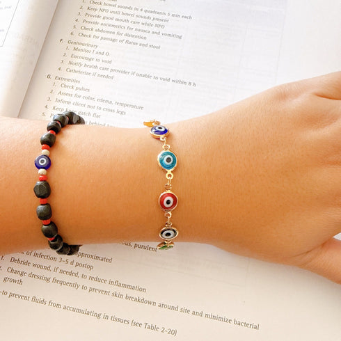 A hand wearing a 14k gold-filled bracelet rests on an open Kaplan Nursing study book.