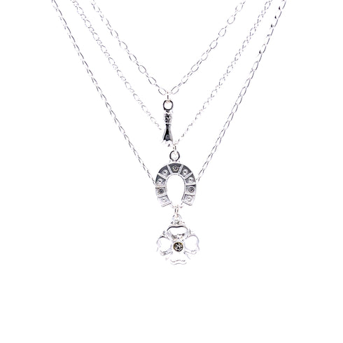 The Good Luck Charms Pendant Stacked Necklace, a 17-inch silver-plated piece, boasts three delightful layers: the top chain with a delicate arrow, the middle featuring a decorated horseshoe, and the bottom highlighting a four-leaf clover with a central gem symbolizing good fortune.