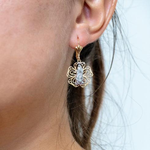 Close-up of a skin-friendly, gold earring from the "Dangling Earrings Our Miraculous Virgin Mary 2 Tones" collection, designed in a floral shape with a central silver element, crafted from 14k gold-filled material, worn on a person's ear.