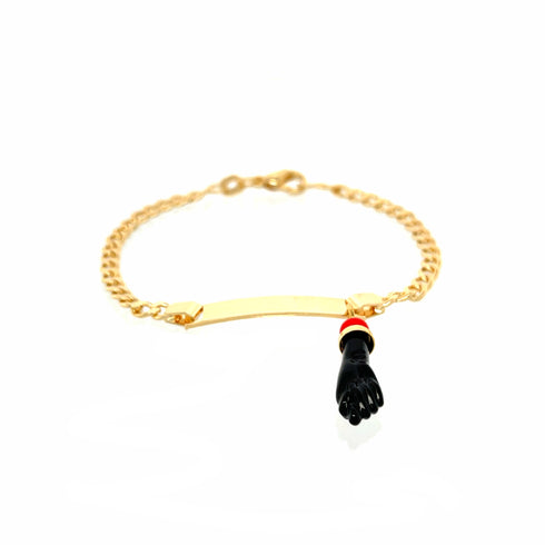 A 14k gold-filled Cuban curb chain bracelet with a plain engraved plate, featuring a black figa hand charm for spiritual protection, adorned with a red and white band around the wrist.