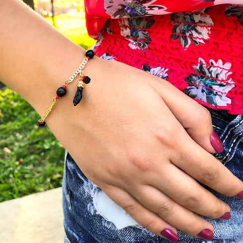 A person wearing a red floral top showcases the Genuine Jet Black Azabache Bracelet and Necklace for Evil Eye on their wrist, embracing the spiritual protection it offers on this sunny day.