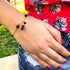 A person wearing a red floral top showcases the Genuine Jet Black Azabache Bracelet and Necklace for Evil Eye on their wrist, embracing the spiritual protection it offers on this sunny day.