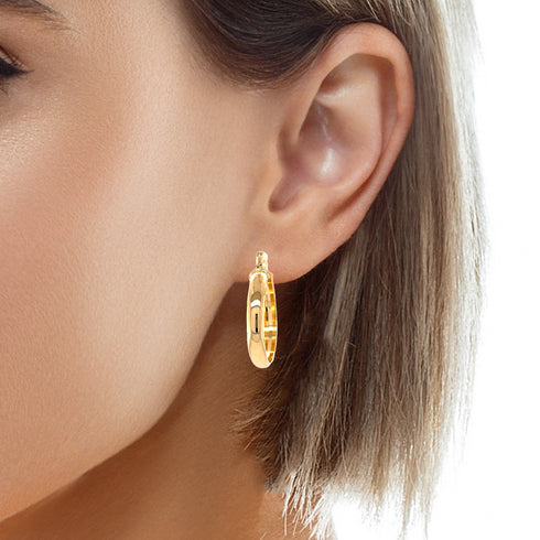 The image showcases a person wearing a round hoop earring that gleams in its 14k gold-filled finish. The 1-inch earring boasts a flat inner side and measures 4mm in width, offering a sleek and uncomplicated design. Free from lead and nickel, this accessory beautifully complements the person's short, straight hair.