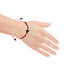 A hand adorned with the Genuine Azabache Crucifix Red Rope Bracelet, an adjustable unisex accessory for women and men, featuring red and black beads, rests on a white background, palm down, showcasing the spiritual protection provided by this jewelry.