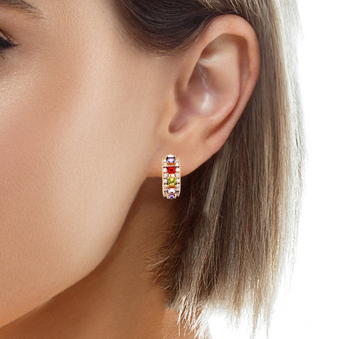 A close-up shows an individual wearing the Multi color Gemstone Zirconia Huggies Earrings rose gold filled. These earrings feature stones in vibrant hues of red, green, orange, purple, and yellow set in rose-gold-filled metal. Designed for sensitive ears, these hypoallergenic earrings beautifully complement the person's short brown hair and elegant profile.