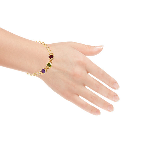 A hand adorned with the "Red Green and Purple Gemstone Link Bracelet 18k Gold Filled" delicately showcases an array of vibrant gemstones. This lead and nickel-free piece elegantly rests on the wrist, highlighting its intricate design against a white background.